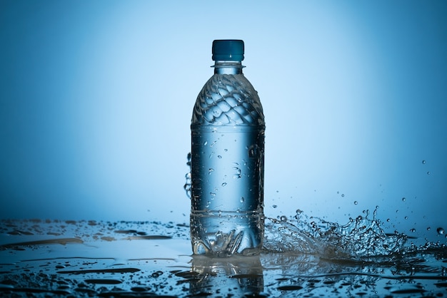 Limpiar el agua dulce derramando y salpicando cerca de la botella de plástico transparente sobre fondo azul.