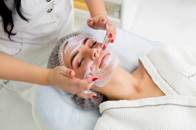 Limpiar la piel con espuma, una mujer hermosa en el salón de belleza de la belleza. Trabajo de cosmetóloga.