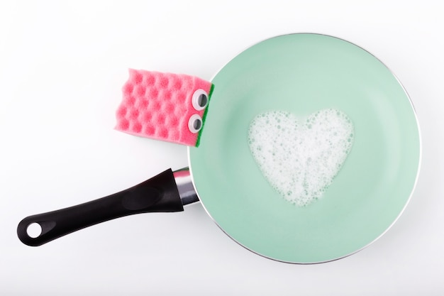 Limpiar los platos sucios con una esponja rosa con detergente.