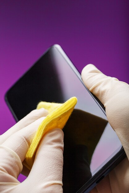 Foto limpiar un teléfono inteligente con una servilleta amarilla de suciedad y virus en guantes de goma