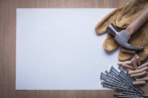 Limpie la hoja de clavos de acero de papel martillo pasadores de madera y guantes de seguridad de cuero en el concepto de construcción de copyspace de tablero de madera