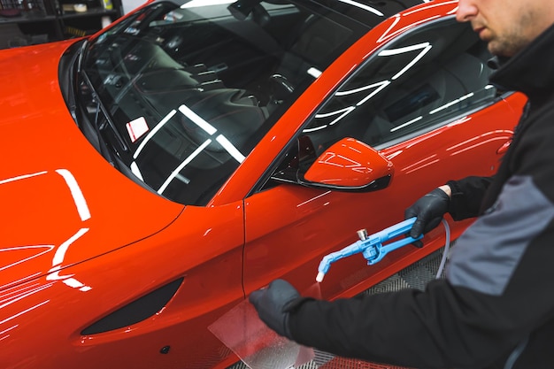 Limpieza de un coche rojo con spray para lavadora en el taller de reparación