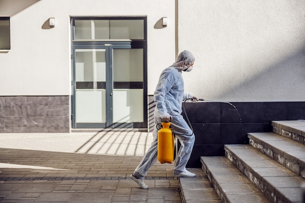 Limpieza y desinfección en el exterior alrededor de los edificios, la epidemia de covid-19. equipos de sesión para los esfuerzos de desinfección. Prevención de infecciones y control de epidemias. e traje y máscara.