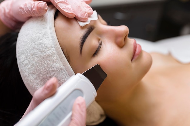 Limpieza facial con depurador de ultrasonidos Mujer que recibe limpieza y peeling facial por ultrasonidos Cosmetología y cuidado de la piel del rostro Tratamiento facial