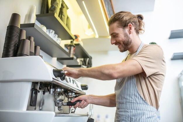 Foto limpieza de filtros, cafetera. adulto joven sonriente hombre informado en el delantal de limpieza de la máquina de café con filtro en el café