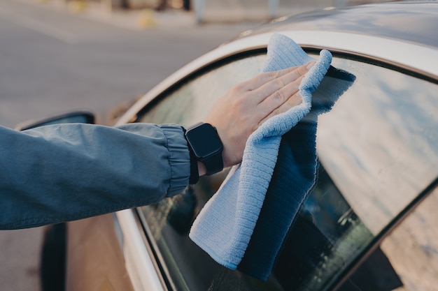 Limpieza de manos masculinas ventana lateral de coche con trapo de microfibra