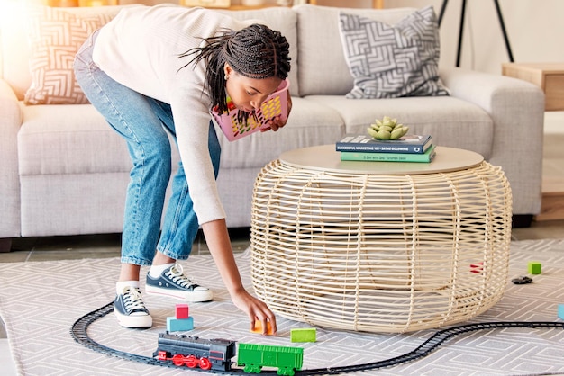 Limpieza de primavera, sala de estar y juguetes para niños, limpieza de una madre de criada en una casa, madre trabajadora de la casa y servicio de limpieza con una mujer negra en un salón, recogiendo el tren de juguete de los niños en la alfombra del piso