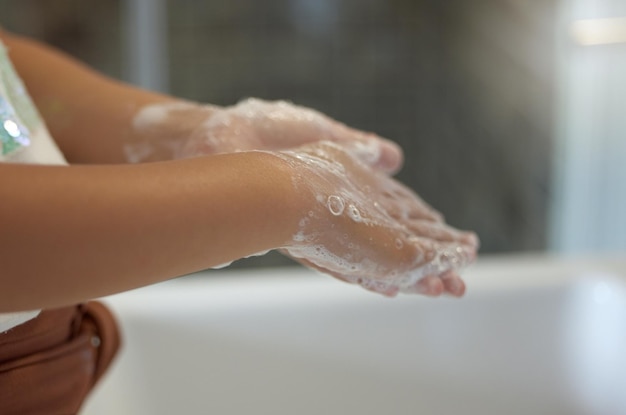 Limpieza y protección contra infecciones por parte de una niña que se lava las manos con jabón de espuma en el baño para la prevención de virus Una niña practica higiene y limpieza enjuagándose las palmas de las manos en el lavabo