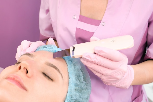 Limpieza ultrasónica del rostro de una mujer joven en un consultorio de cosmetología.