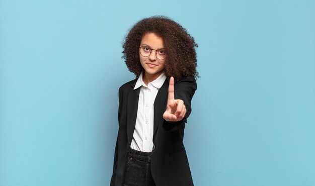 Linda adolescente afro sorrindo com orgulho e confiança fazendo a pose número um triunfantemente