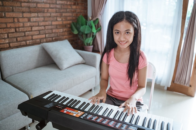 Linda adolescente asiática tocando um instrumento de piano