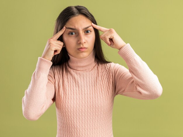 Foto linda adolescente carrancuda olhando para a frente levanta as sobrancelhas fazendo um gesto de pensar isolado na parede verde oliva