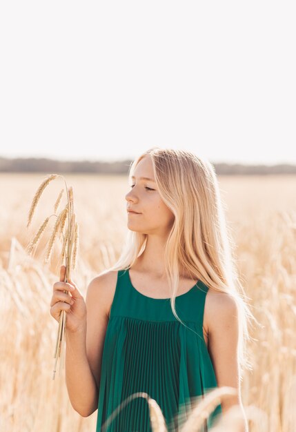 Linda adolescente com longos cabelos brancos caminhando por um campo de trigo em um dia ensolarado