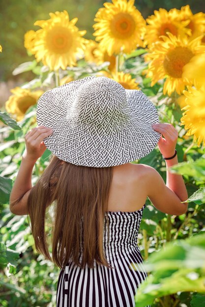 Linda adolescente com um chapéu de abas largas em um campo de girassóis. Conceito de horário de verão.