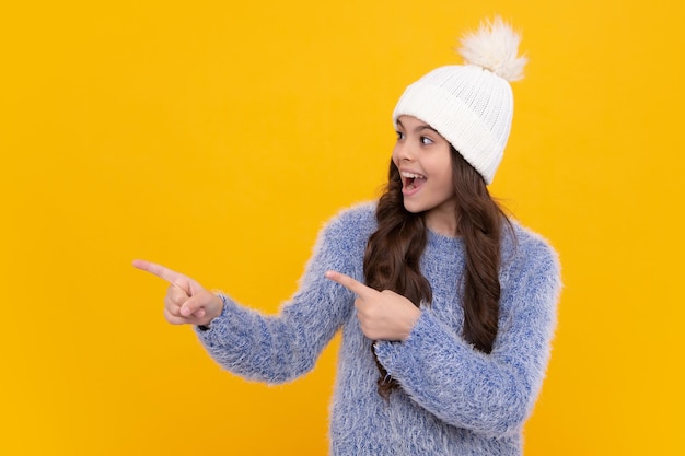 Linda adolescente com um chapéu de inverno e um suéter quente Uma criança em um fundo amarelo isolado Rosto animado emoções alegres de adolescente