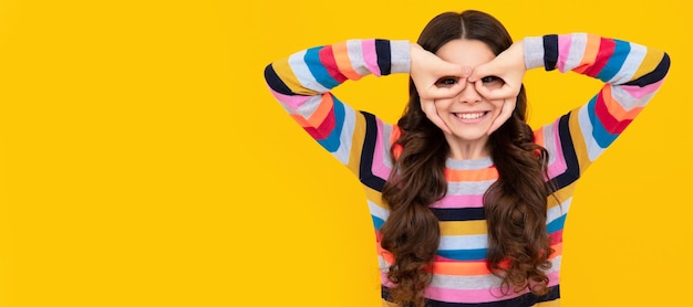 Linda adolescente criança olhar especificações de dedo okey símbolo formas bobas figuras isoladas em fundo amarelo rosto de criança cartaz horizontal menina adolescente isolado retrato banner com espaço de cópia