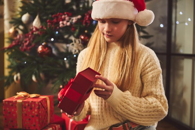 Linda adolescente desenvolviendo el regalo de Navidad en el interior