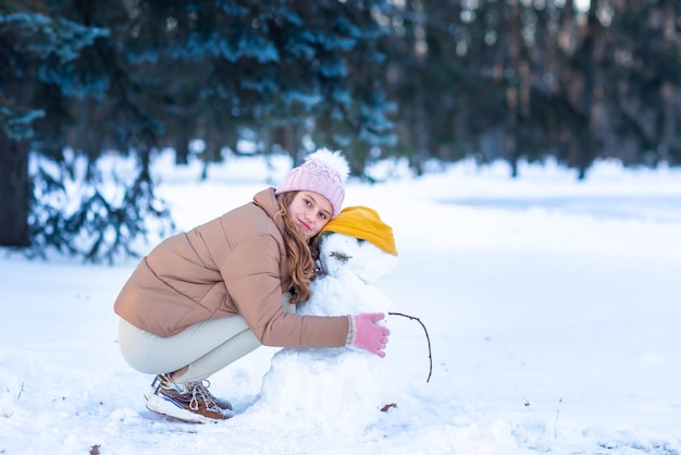 Una linda adolescente divirtiéndose jugando a hacer muñecos de nieve en el bosque nevado de invierno