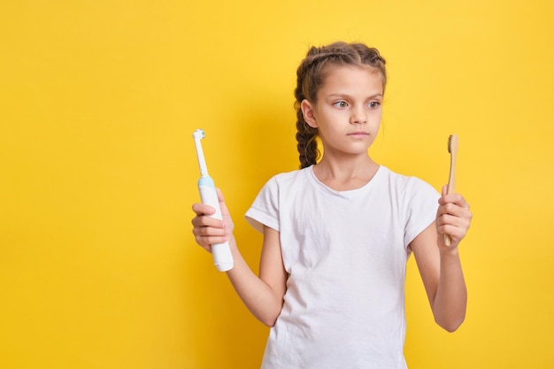 Linda adolescente con peinado de coletas elige entre cepillo de dientes de bambú y eléctrico