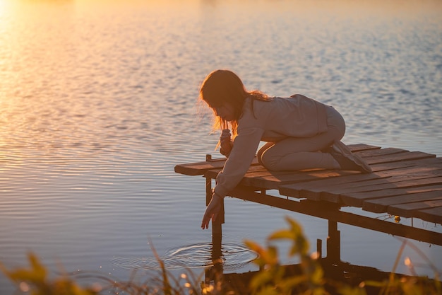 Una linda adolescente sentada en un puente del muelle junto al río al atardecer