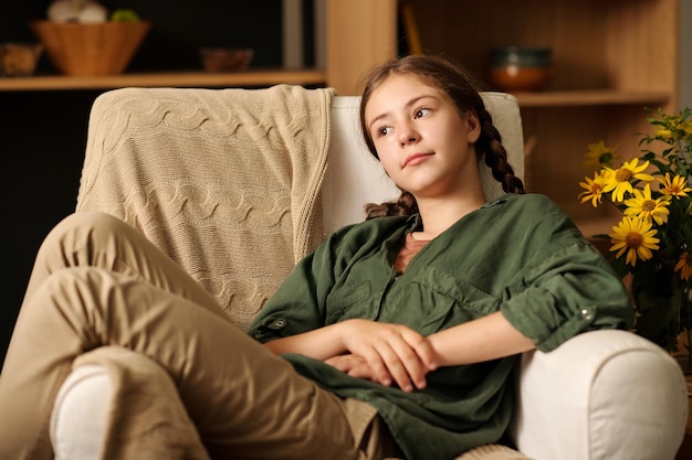 Linda adolescente serena em roupas casuais relaxando em uma poltrona confortável