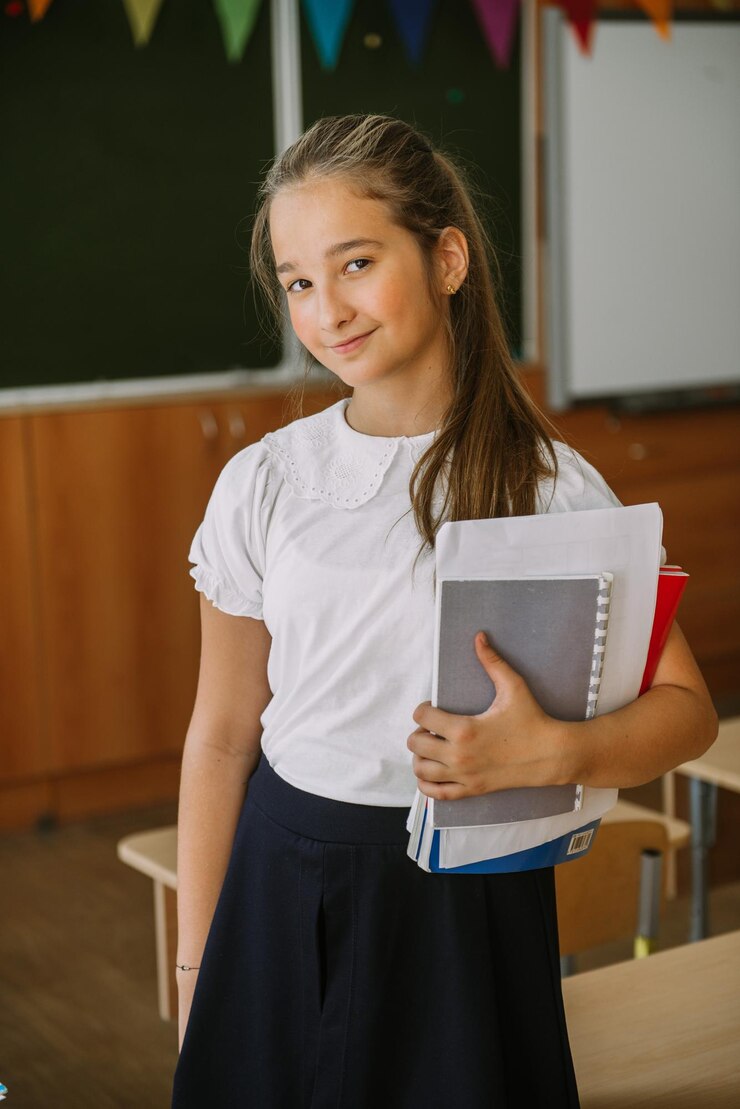una linda adolescente sonriente posando con cuadernos en el aula