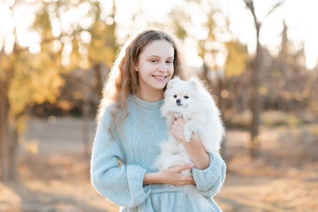 Linda adolescente sorridente de 15 a 16 anos segurando um cachorrinho spitz branco fofo juntos durante o outono