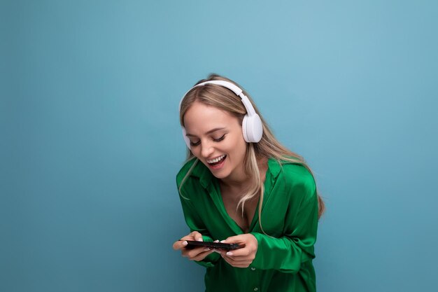 Linda alegre atractiva mujer joven rubia en auriculares con un teléfono inteligente en sus manos en un azul