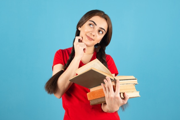 Linda aluna em t-shirt vermelha, lendo atentamente o livro na parede azul.