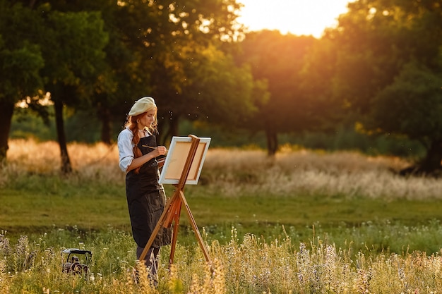 Linda artista feminina pintura ao pôr do sol na natureza