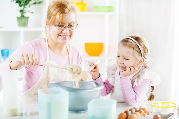 Linda avó feliz aprendendo sua neta assando em uma cozinha.