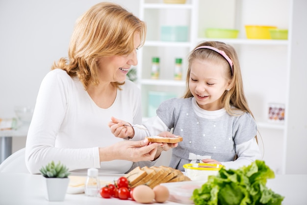 Linda avó feliz e sua neta fofa fazendo sanduíche na cozinha.