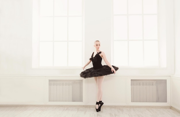 Linda bailarina graciosa em vestido de cisne preto. Jovem bailarina praticando antes da apresentação em tutu preto, estúdio de dança clássica, espaço de cópia