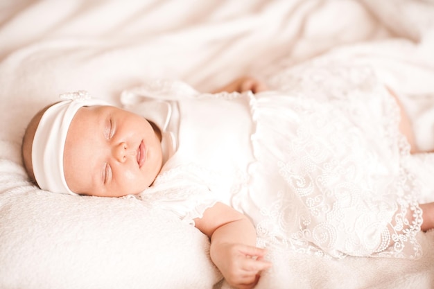 Una linda bebé dormida usa un elegante vestido blanco y una diadema en la cama