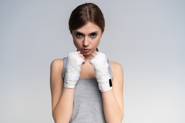 Linda boxer vestindo roupas esportivas e luvas praticando no estúdio em cinza.