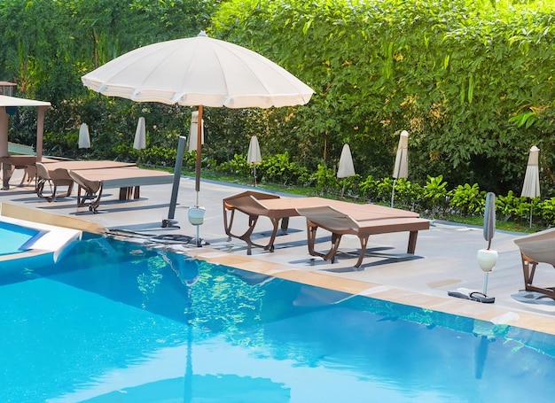 Linda cadeira vazia com guarda-chuva ao redor da piscina ao ar livre no hotel resort para viagens de férias