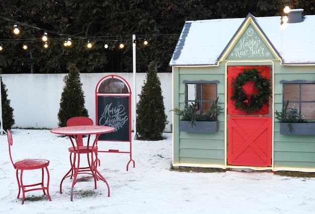 Linda casa de juegos privada de madera pintada de verde rojizo en el jardín de la casa decorada con corona de Navidad al aire libre en la fría noche de la bobinadora de nieve