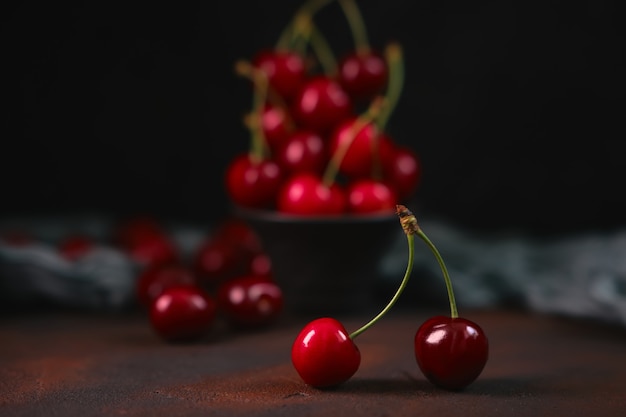 Linda cereja dupla em primeiro plano e cerejas vermelhas frescas e doces em uma tigela de barro preto em uma superfície escura com gotas de água