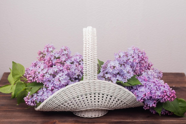 Linda cesta de vime vintage branca em uma mesa de madeira Flores lilás em uma cesta retrô