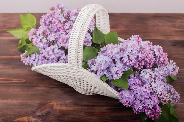 Linda cesta de vime vintage branca em uma mesa de madeira Flores lilás em uma cesta retrô