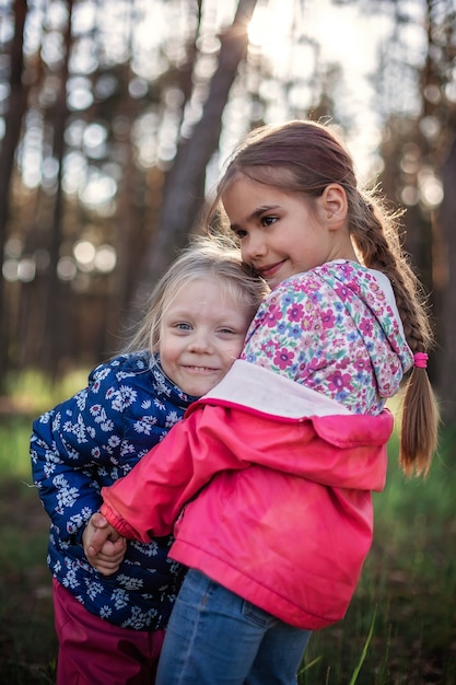 Linda chica abrazando a su hermana pequeña con amor y ternura durante su caminata en el bosque en otoño, día nacional del abrazo y la amistad, estilo de vida informal, al aire libre