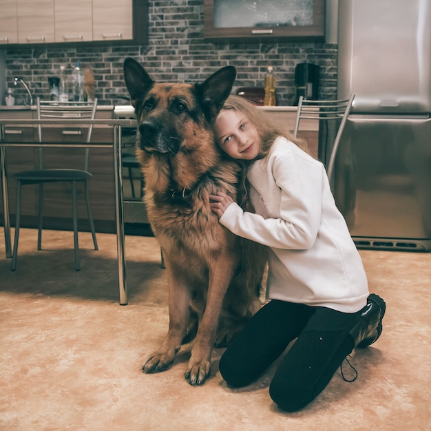 Linda chica abrazando a su mascota pastor alemán en la cocina de casa. amadas mascotas