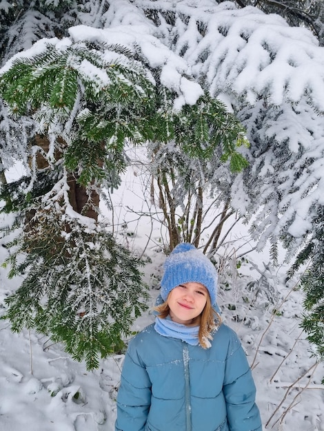 Una linda chica con un abrigo azul bajo un abeto cubierto de nieve