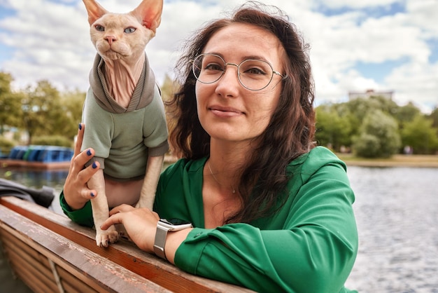 Linda chica acariciando a un gato peludo al aire libre Sentado en un banco de madera con árboles verdes y fondo de río Amor a los animales