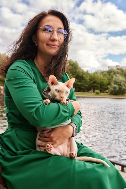 Linda chica acariciando a un gato peludo al aire libre Sentado en un banco de madera con árboles verdes y fondo de río Amor a los animales