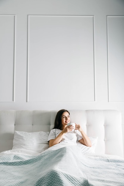 Linda chica acostada con la taza de café en la cama