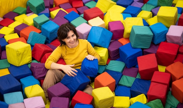 Linda chica acostada en trampolín coloridos cubos y sonriente joven disfrutando de entretenimientos en pla