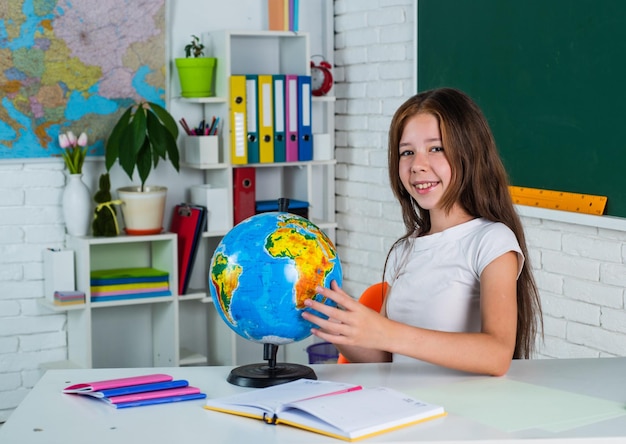 Linda chica adolescente cerca de pizarra con globo de geografía regreso a la escuela