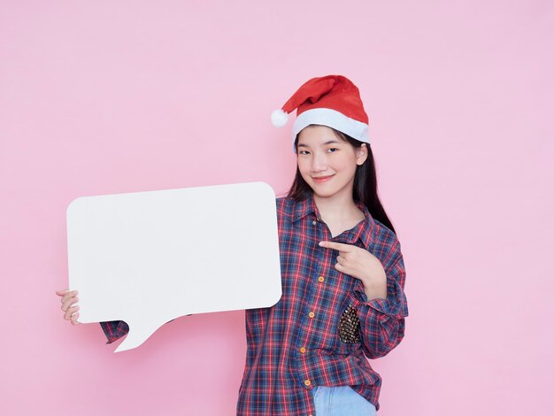 Linda chica adolescente con sombrero de santa claus en cartel en blanco sobre fondo rosa.