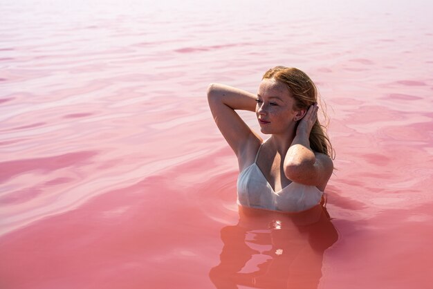 Linda chica adolescente con un vestido blanco en el agua de un increíble lago rosa